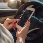 Ways You Can Minimize Distracted Driving - Mockup image of woman hand using mobile smartphone with blank screen while driving car and leaving home. clipping path.