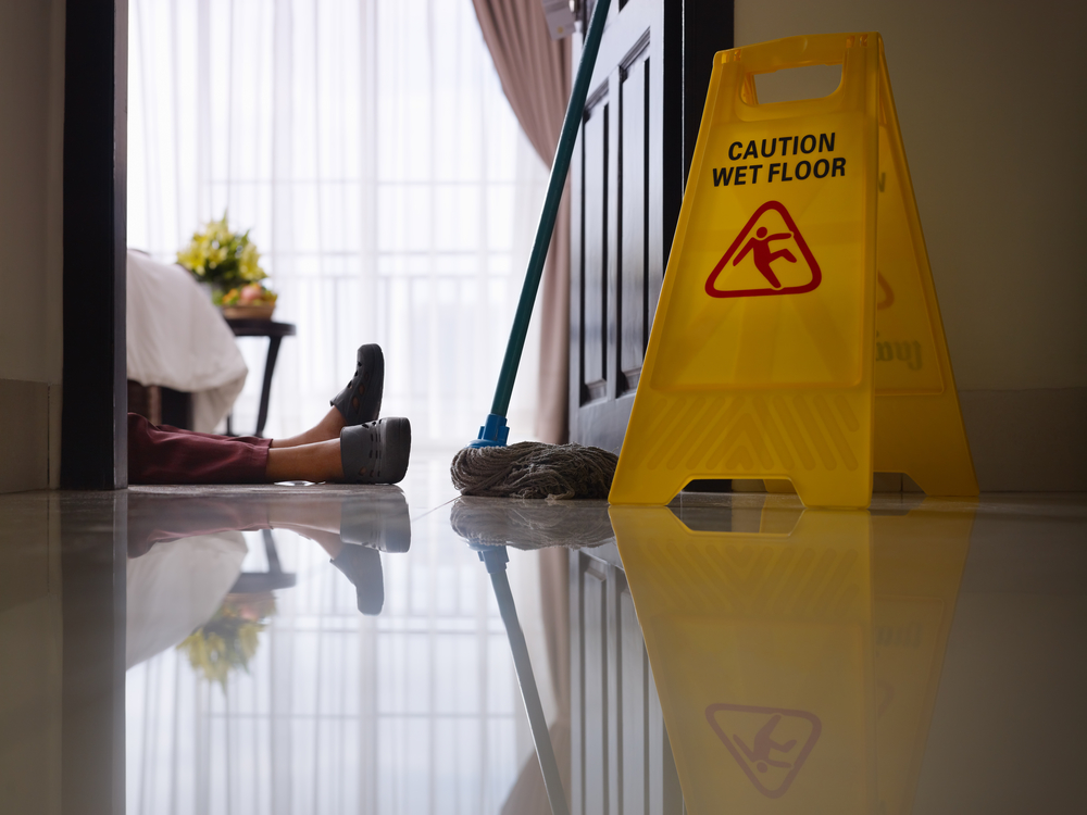 A person lying on the ground next to a caution sign before calling a Slip and Fall Lawyer Menomonee Falls WI